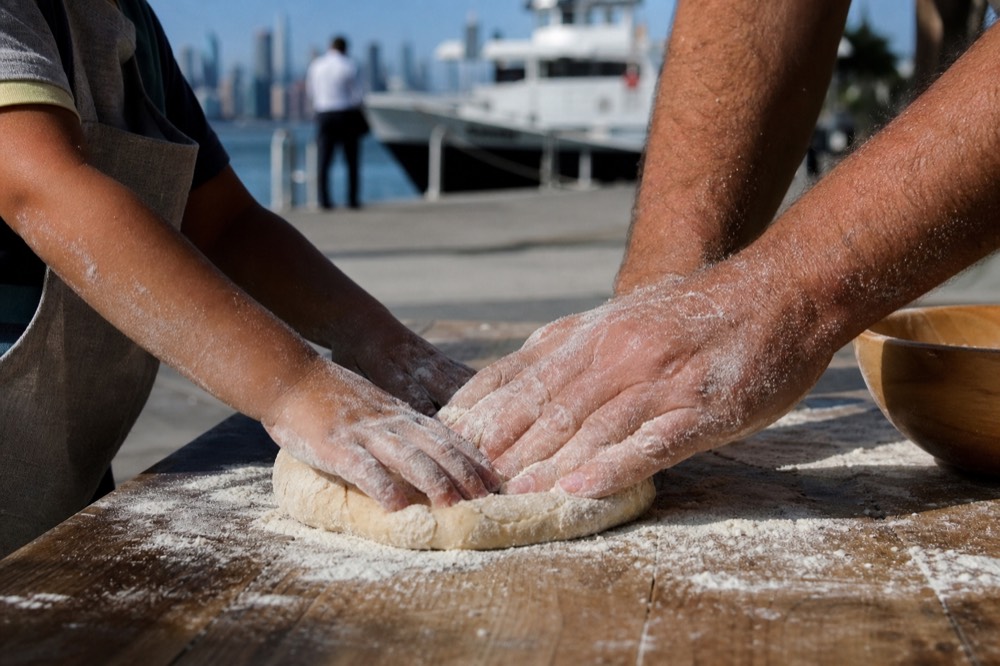 A child's flour-covered hands pressing dough beside an adult's on a rustic wooden table