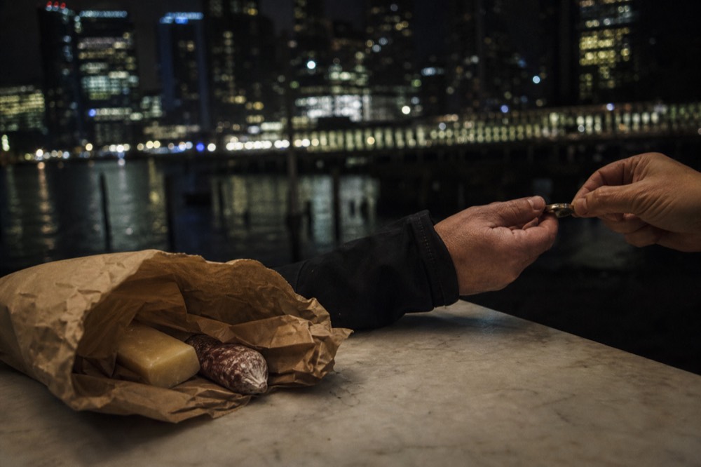 Paper bag of cheese and cured meat on a market counter, hands passing change across the marble