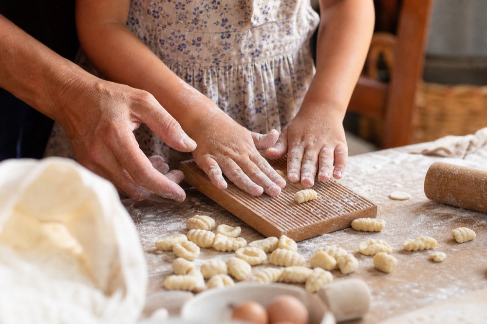 Small hands pressing pasta shapes at a family cooking table