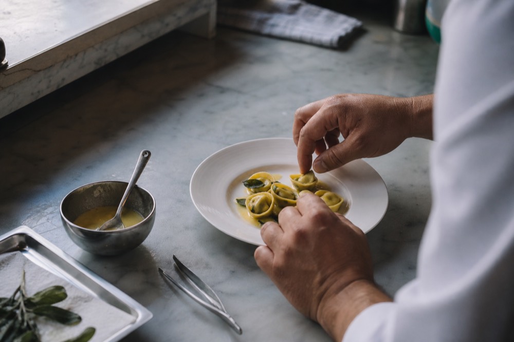 A chef demonstrating ravioli folding at a marble bench