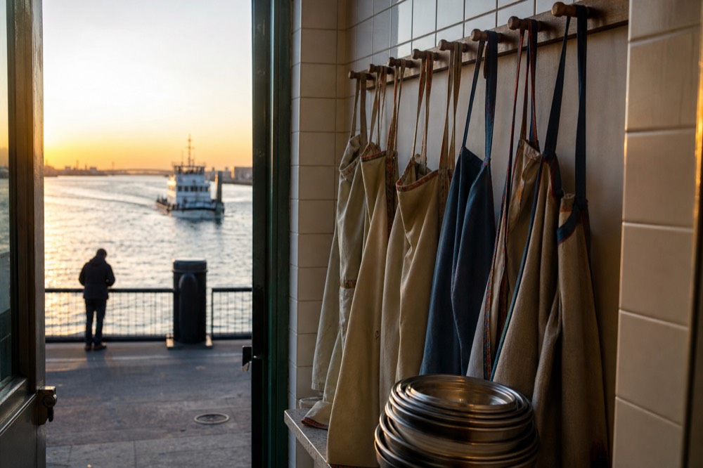 A neat row of child-sized aprons hanging on wooden pegs beside a stack of small mixing bowls in a tiled kitchen entrance