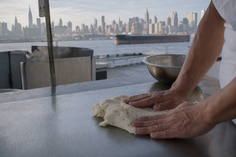 Hands pressing a pale rice and corn flour dough on a clean stainless steel work surface, no wheat flour visible anywhere in the frame