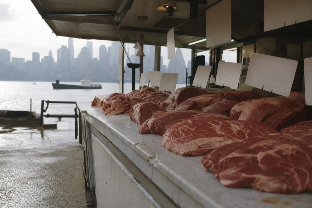 Butcher's counter in a covered market with cuts of beef on white marble and hand-lettered blank price cards above