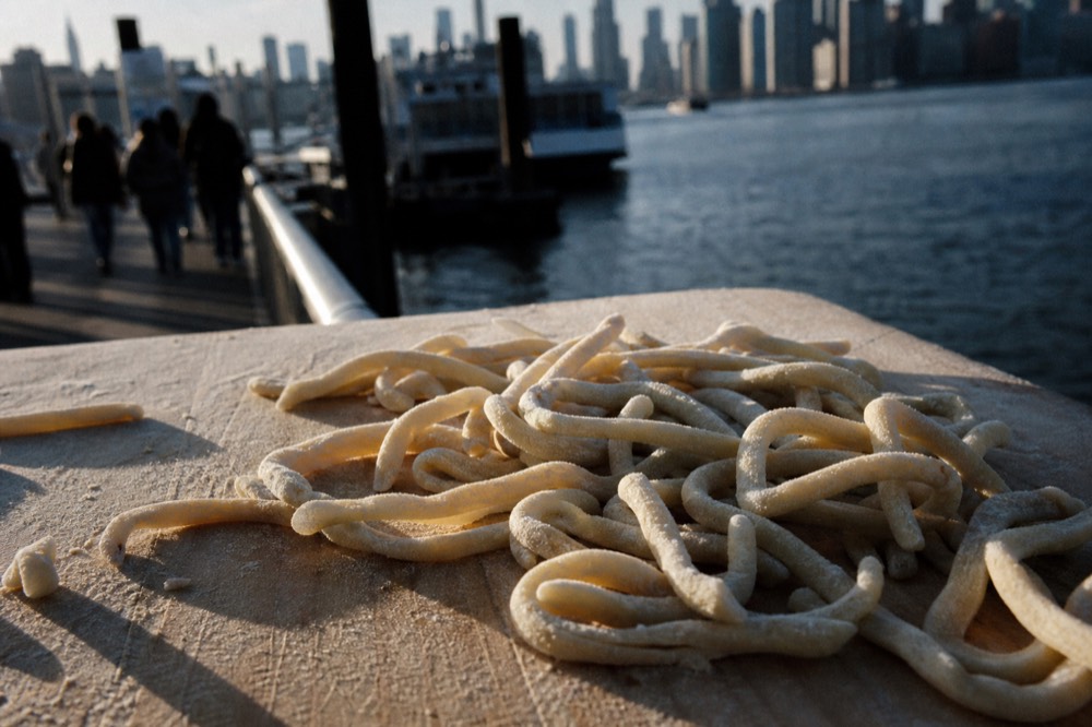 Close crop of thick hand-rolled pici pasta on a semolina-dusted board, uneven and clearly handmade