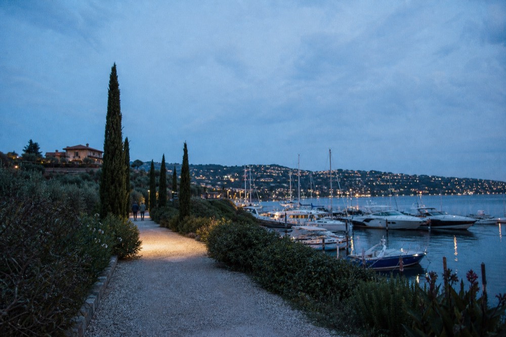 A gravel drive lined with cypress trees leading to a terracotta-roofed Tuscan farmhouse under a wide blue sky